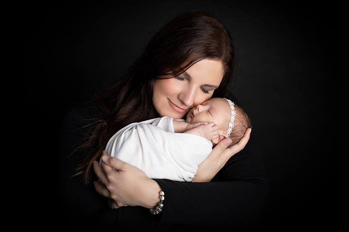 Newbornshooting Düsseldorf: Mama hält verliebt ihr Neugeborenes in den Armen und schmiegt mit geschlossenen Augen ihren Kopf an das Baby.