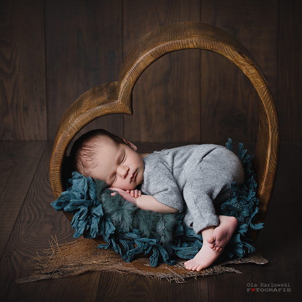 Neugeborenenshooting in Düsseldorf: Ein Baby schläft in enem herzförmigen Rahmen aus Holz. Das Neugeborene ist dabei auf eine weiche blaue Decke gebettet.