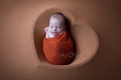 Newbornshooting Düsseldorf: Baby liegt nach Pucken friedlich schlafend in einer herzförmigen Schüssel auf weichem Stoff. Fotografin A. Ola Karlowski